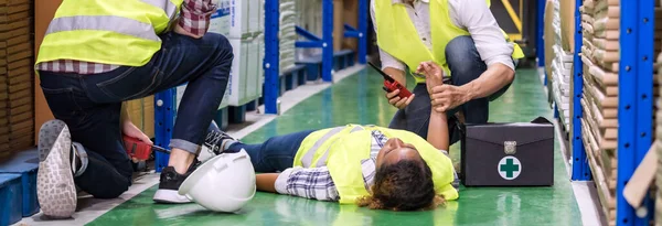 全景仓库的工作人员在工作时意外地躺在仓库地板上对他的同事进行急救 用于工业安全第一和商业保险概念 — 图库照片