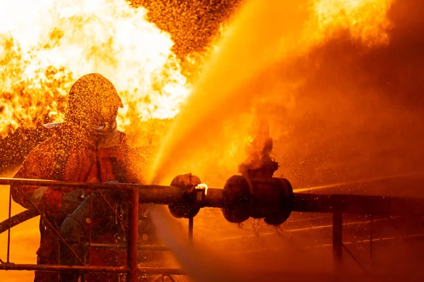 Firefighter using water fog type fire extinguisher to fighting with the fire flame from oil pipeline leak and explosion on oil rig and natural gas station. Firefighter and industrial safety concept.