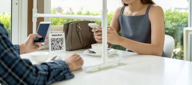 Panoramik Asyalı müşteriler QR kod çevrimiçi menüsünü tarıyor. COVID-19 salgınından sonra müşteriler restoranda yeni normal yaşam tarzı için sosyal uzaklık masasına oturdu.