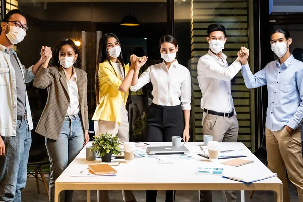 ビジネスマンは 夜の会議室での新しい通常のオフィスライフスタイルでコロナウイルスCovid 19の感染を減らすために握手の代わりに別の挨拶を行います 彼らは保護顔マスクを着用 ストック画像