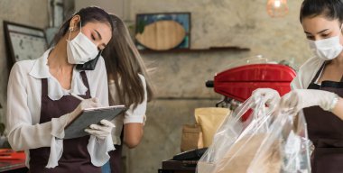 Panoramik Asyalı garson, şehir kapatılırken paket servis ya da kaldırım kenarındaki servis siparişleri için cep telefonundan sipariş alıyor. Coronavirus COVID-19 salgınını önlemek için yüz maskesi takıyorlar..