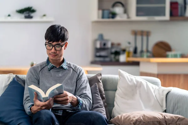 Feliz Asiático Joven Adulto Hombre Sentado Sofá Sala Estar Leyendo —  Fotos de Stock