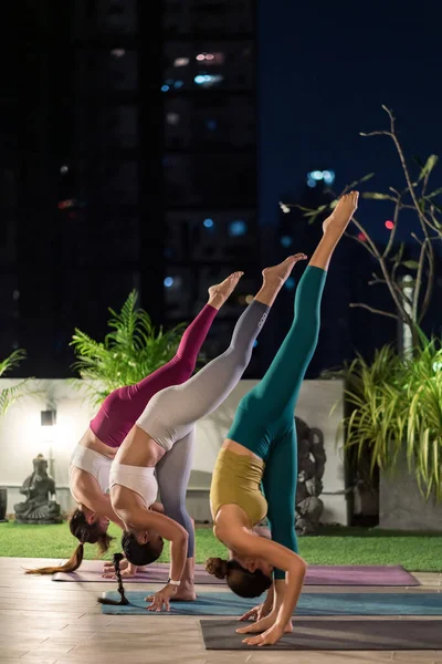 都会の中でヨガを練習しているスポーツウェアパンツ姿のアジア系女性たちが イルミネーションの夜を背景に距離を置きながらアパートメントに閉じ込められている フィットネス 健康的なライフスタイルのコンセプト — ストック写真