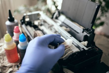 Yazıcıyı mürekkeple dolduruyorum. Eldivenli bir el boş bir toner kutusu tutar. Evdeki ekipmanların bakımı ve bakımı. Kapat.