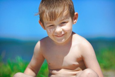 Mutlu çocuk güneşli bir günde sahilde oturuyor. Beyaz Kafkas çocuk güneşte güneşleniyor.