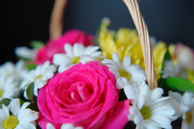 Hasır sepetin içinde bir buket çiçek ve koyu bir arka planı var. Kutlama için çiçek düzenleme