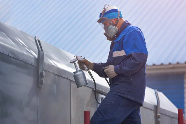 Endüstriyel işler. Kompresör silahından çıkan metal ürünlerin hazırlanması. Tulumlu ve solunum cihazlı bir işçi merdivenlerde durur ve bir kamyon römorku ya da metal bir arabanın vücudunu boyar. Yükseklikte çalış