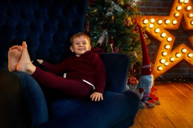 Neşeli ve mutlu bir çocuk sandalyede yatıyor. Noel tatili ve hediye bekleyen bir çocuk.