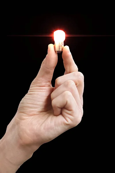 A man\'s hand holds a small glowing light bulb in his fingers. Isolate on a black background. Concept of an idea or inspiration. Blank for design