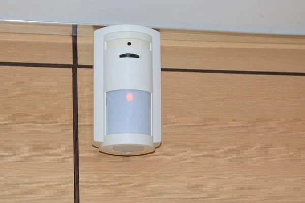 Motion sensor of the security alarm system. A white volume sensor hangs on the wall in a room or office.