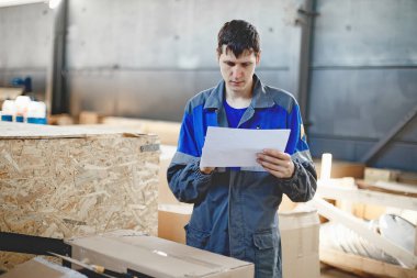 Depodaki malların kabulü. Tulumlu genç bir işçi malları envantere göre kontrol ediyor..