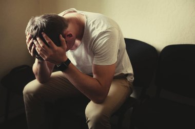 Erkek problemleri. Genç bir adam sandalyeye oturur ve kafasını ellerinin arasına alır..