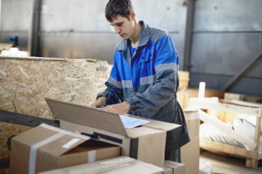 Depodaki malların kabulü. Tulumlu genç bir işçi malları envantere göre kontrol ediyor..