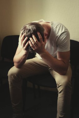 Erkek problemleri. Genç bir adam sandalyeye oturur ve kafasını ellerinin arasına alır..