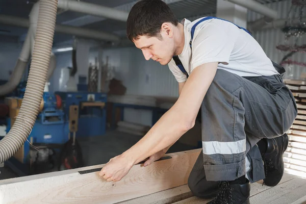 Genç bir adam bir marangozhanede çalışıyor. Bir çalışan ahşabı cetvelle ölçer. — Stok fotoğraf