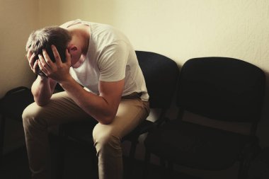 Erkek problemleri. Genç bir adam sandalyeye oturur ve kafasını ellerinin arasına alır..