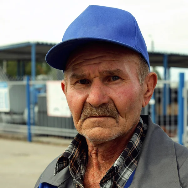 A tired and sad old man in a baseball cap with copy space looks at the camera.Portrait of an old and sad worker outdoors