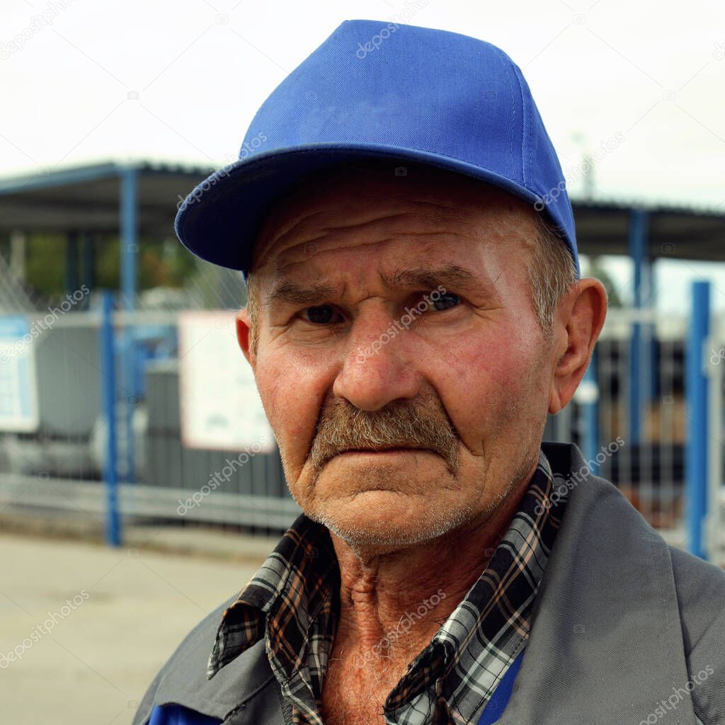 A tired and sad old man in a baseball cap with copy space looks at the camera.Portrait of an old and sad worker outdoors
