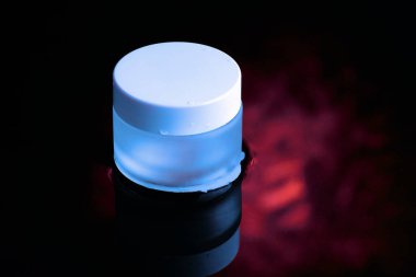 Beyaz kapaklı mavi cam bir kavanoz suyun içinde duruyor. Karanlık tema. 