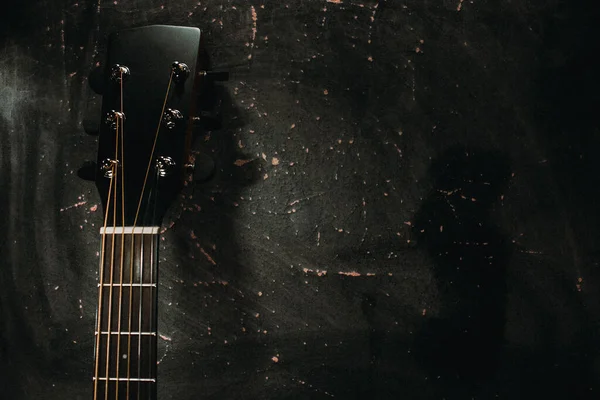 Akustik bir gitar, karanlık bir arka plana karşı duvara dayanır.. — Stok fotoğraf