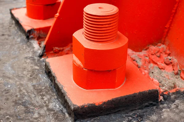 Czerwony metalowy wspornik jest przykręcany do betonowej podstawy dużymi śrubami. Mocowanie wieży lub wieży do podłoża. — Zdjęcie stockowe