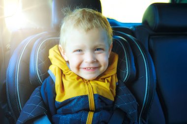 Sarışın bir çocuk çocuk çocuk koltuğunda oturur ve gülümser. Arabadaki mutlu çocuk bu. Araba kullanırken dikkat ve güvenlik.