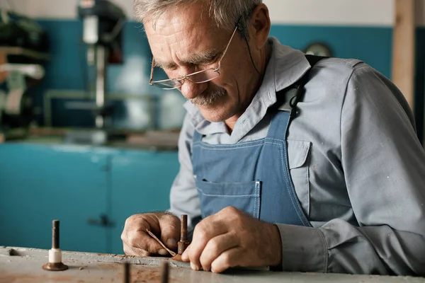 Старый мастер в очках работает в мастерской — стоковое фото
