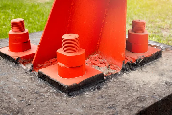 Czerwony metalowy wspornik jest przykręcany do betonowej podstawy dużymi śrubami. Mocowanie wieży lub wieży do podłoża. — Zdjęcie stockowe
