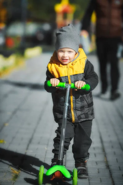 Bambino felice ed emotivo cavalca uno scooter a tre ruote nel parco lungo il percorso. — Foto Stock