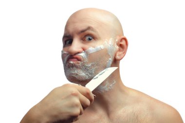 Kel beyaz bir adam sakalını parlak bir mutfak bıçağıyla tıraş ediyor. Tıraş köpüğüyle bir erkek yüzü.