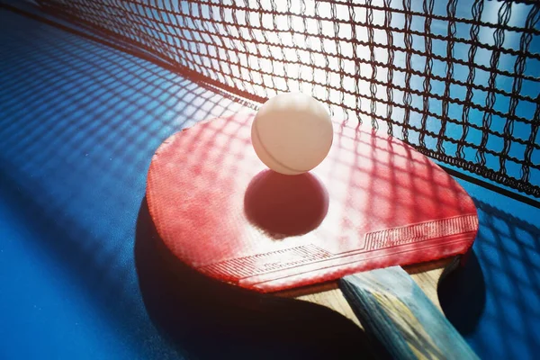 A red table tennis racket and a white ball lie on the surface of the table next to the net. Sports game