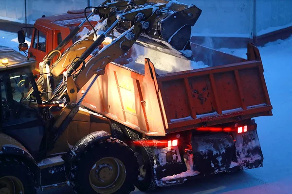 Una excavadora carga nieve en la parte trasera de un camión volquete por la noche. — Foto de Stock