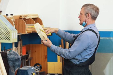 Gözlüklü yaşlı bir marangoz mezura ile tahta bir parça ölçer..