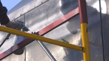 Kompresör silahından çıkan metal ürünlerin hazırlanması. Tulumlu bir işçi kargo karavanının gövdesini boyar.
