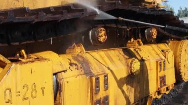 İşçi, basınç altında bir su tabancasıyla buldozerin izlerini yıkar. Bu ağır makineleri yıkamak için bir hizmet.