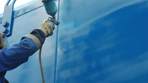 Un trabajador con un mono y un respirador pinta el cuerpo de un remolque de carga o un coche de metal en azul. — Vídeos de Stock