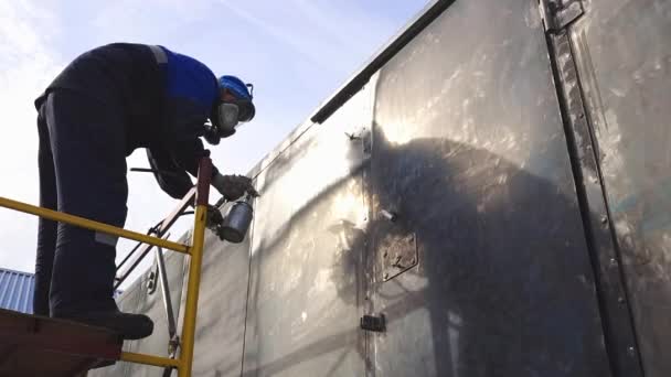 Industrial work. Priming of metal products from the compressor gun. A worker in overalls and a protective mask paints the body of a truck trailer or a metal car. — Stock Video