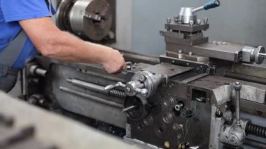 Makine atölyesindeki makine aletlerinin önlenmesi ve bakımı. Tulumlu bir işçi, metalle çalışmak için torna tezgahı kurar.