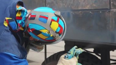 Solunum cihazındaki bir araba tamircisi ve renkli bir bandana kompresör silahından metal bir araba yaptırıyor. Üretim işi dışarıda..