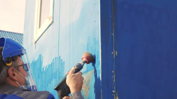 Pracownik w masce ochronnej czyści duże urządzenia szlifierką. Mężczyzna przygotowuje przyczepę do malowania. — Wideo stockowe