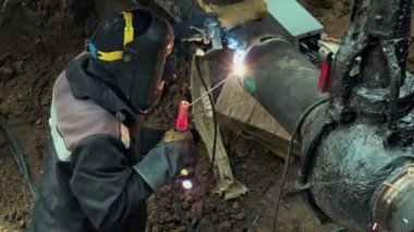 Maskeli bir kaynakçı gündüz vakti bir boruyla siperde çalışır. Ana gaz boru hattının kaynak işlemi.