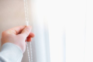 Bir adam güneş ışığından dolayı pencerelerin perdelerini kapatır. Panjur üreticisi için reklam fotoğrafı ve kopyalama alanı. Yumuşak odak