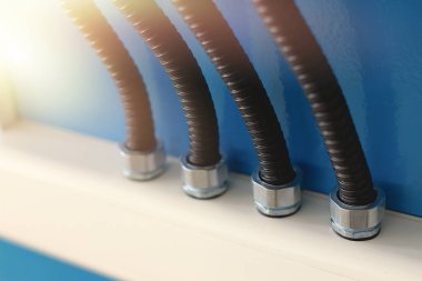 Bükülmüş korumadaki elektrik kabloları kablo kanalına fındık yoluyla bağlanıyor. Arka planda ışıklandırma ve kopyalama alanı olan endüstriyel arkaplan.