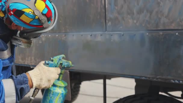 A worker in uniform and gloves paints a metal trailer with a compressor gun. Service for painting heavy machinery. — Wideo stockowe