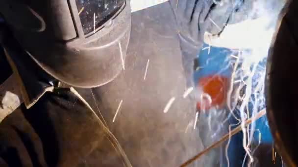 Um soldador mascarado trabalha na loja. Faíscas e flashes ao soldar metal. Retrato de um soldador — Vídeo de Stock