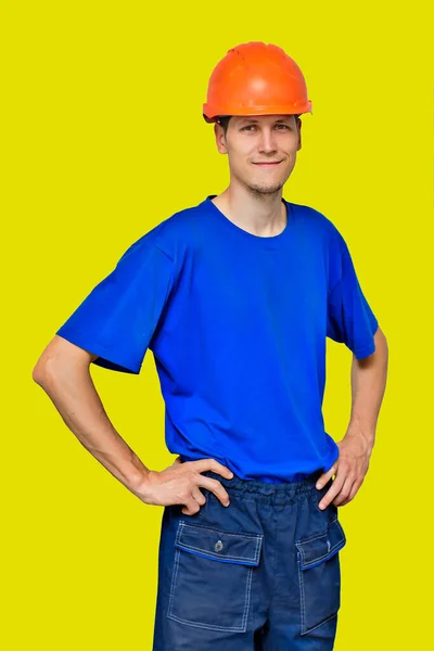 Retrato de um jovem bonito em um capacete de construção e roupas de trabalho Isolado em um fundo amarelo.. — Fotografia de Stock