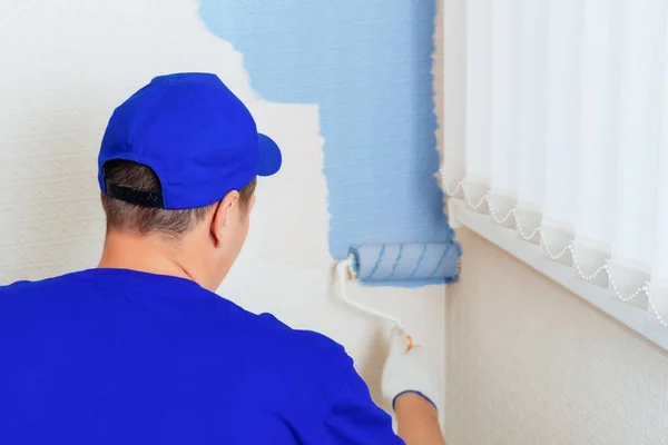 Επισκευή και αποκατάσταση χώρων. Πορτρέτο ενός ζωγράφου σπιτιού και ενός κυλίνδρου χρώμα ζωγραφική στον τοίχο σε μπλε. — Φωτογραφία Αρχείου