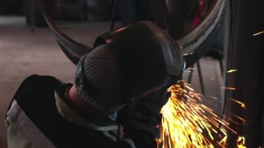 Kaynakçı kaynak makinesini çalıştırır ve kıvılcımlar saçar. Kaynaklı metal boru halkaları işleniyor.