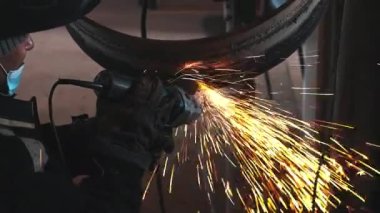 Kaynakçı kaynak makinesini çalıştırır ve kıvılcımlar saçar. Kaynaklı metal boru halkaları işleniyor.