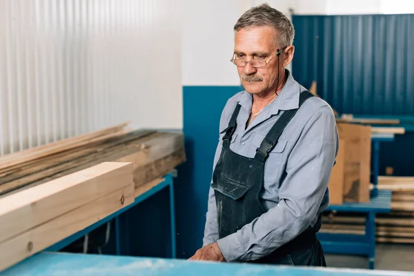 Yaşlı bir marangoz ya da marangoz portresi marangozların atölyesinde ahşap tahtalarla çalışıyor.. — Stok fotoğraf